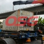 Crane lifting a refrigerated shipping container onto a truck.