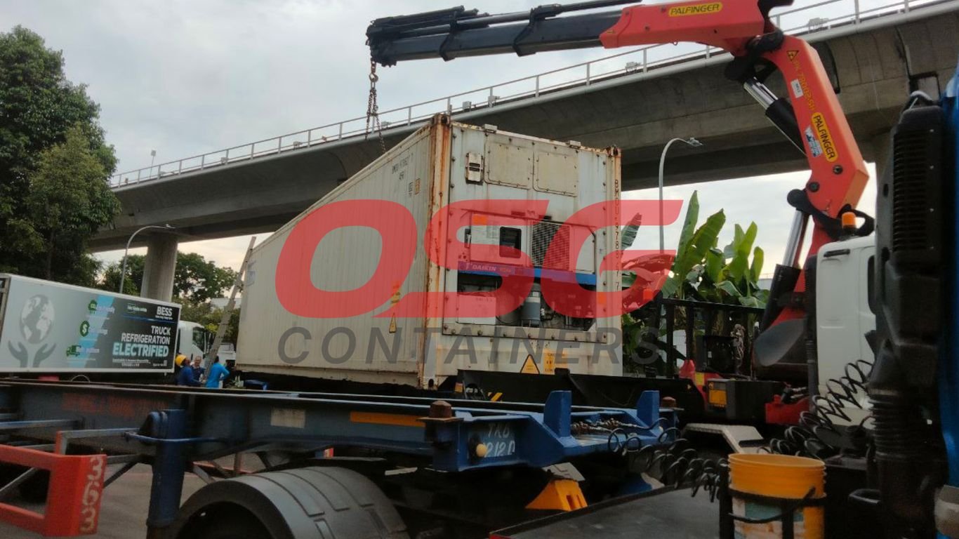 Crane lifting a refrigerated shipping container onto a truck.
